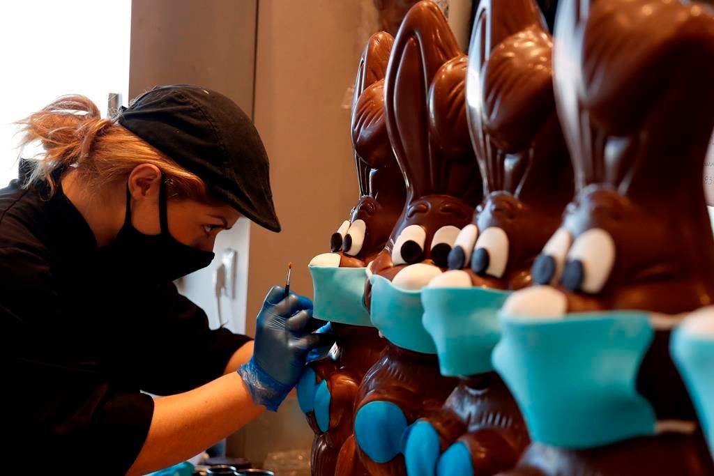 An employee of cake shop prepares chocolate Easter bunnies with masks in Lykovrisi, northern Athens, on Wednesday, April 8, 2020.