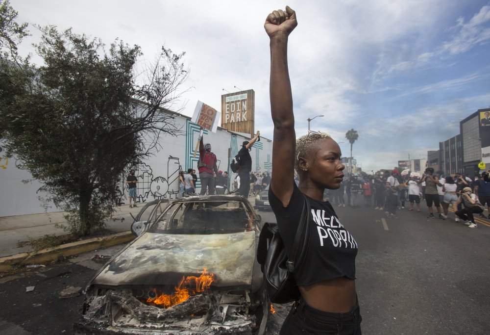 A protester poses for photos next to a burning police vehicle in Los Angeles, Saturday, May 30, 2020, during a demonstration over the death of George Floyd. a black man who was killed in police custody in Minneapolis on May 25.