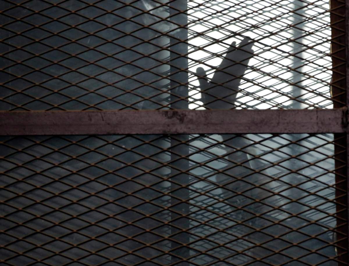 In this Aug. 22, 2015 file photo, a Muslim Brotherhood member waves his hand from a defendants cage in a courtroom in Torah prison, southern Cairo, Egypt.