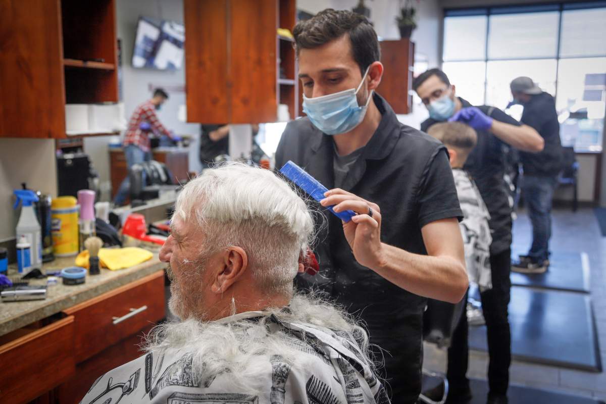 Barber Salim Alhaj, cuts the hair of client John Gee, of Calgary, who came to the Kingsview Barbershop on its reopening in Airdrie, Alta., Thursday, May 14, 2020, amid the COVID-19 pandemic.