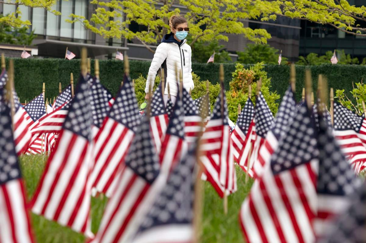 A woman wears a mask to protect agains coronavirus, walks through a field of flags ahead of Memorial Day, Saturday, May 23, 2020, in the Seaport District in Boston.