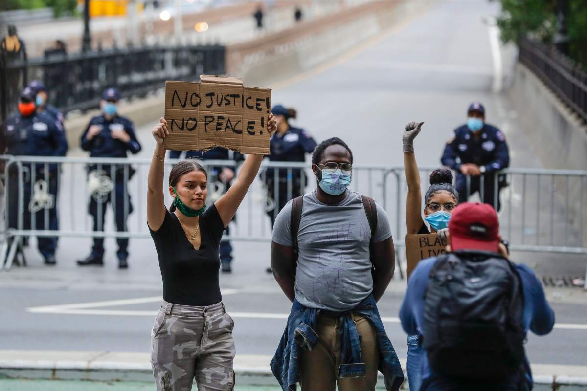 Protesters pose for photos near police officers blocking the entrance to the Brooklyn Bridge during a rally Thursday, May 28, 2020, in New York. (AP Photo/Frank Franklin II)
