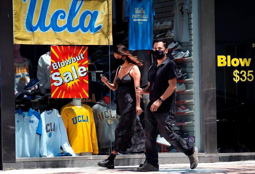 A couple wearing protective masks from the coronavirus walk down the street in the Westwood section of Los Angeles on Friday, May 15, 2020.