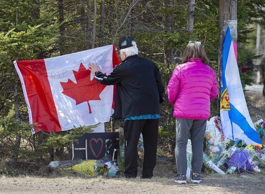 A couple place a flag at a memorial in Portapique, N.S. on Wednesday, April 22, 2021.