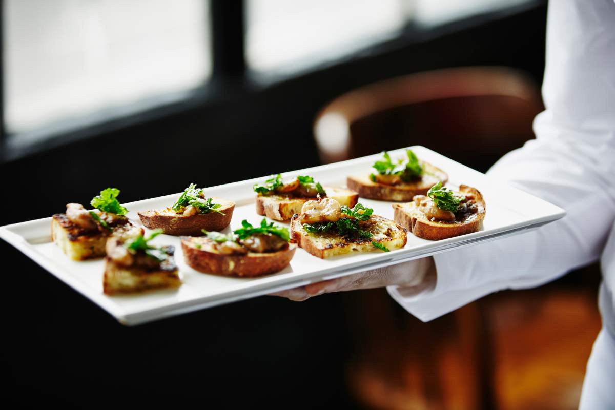 Waitress holding platter of appetizers of smoked bone marrow and crispy organic parsley bruschetta.