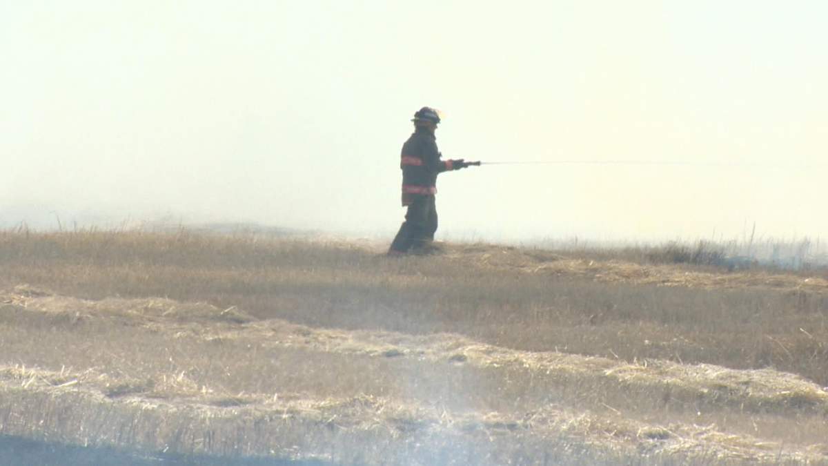 A member of the Saskatoon Fire Department battles a grass fire near Highway 14.