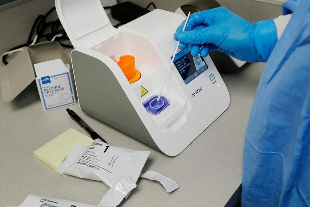 FILE - In this April 10, 2020, file image made from video, a lab technician dips a sample into the Abbott Laboratories ID Now testing machine at the Detroit Health Center in Detroit. Federal health officials are warning about potential accuracy problems with the rapid test for COVID-19 used at thousands of hospitals, clinics and testing sites across the U.S., including the White House.