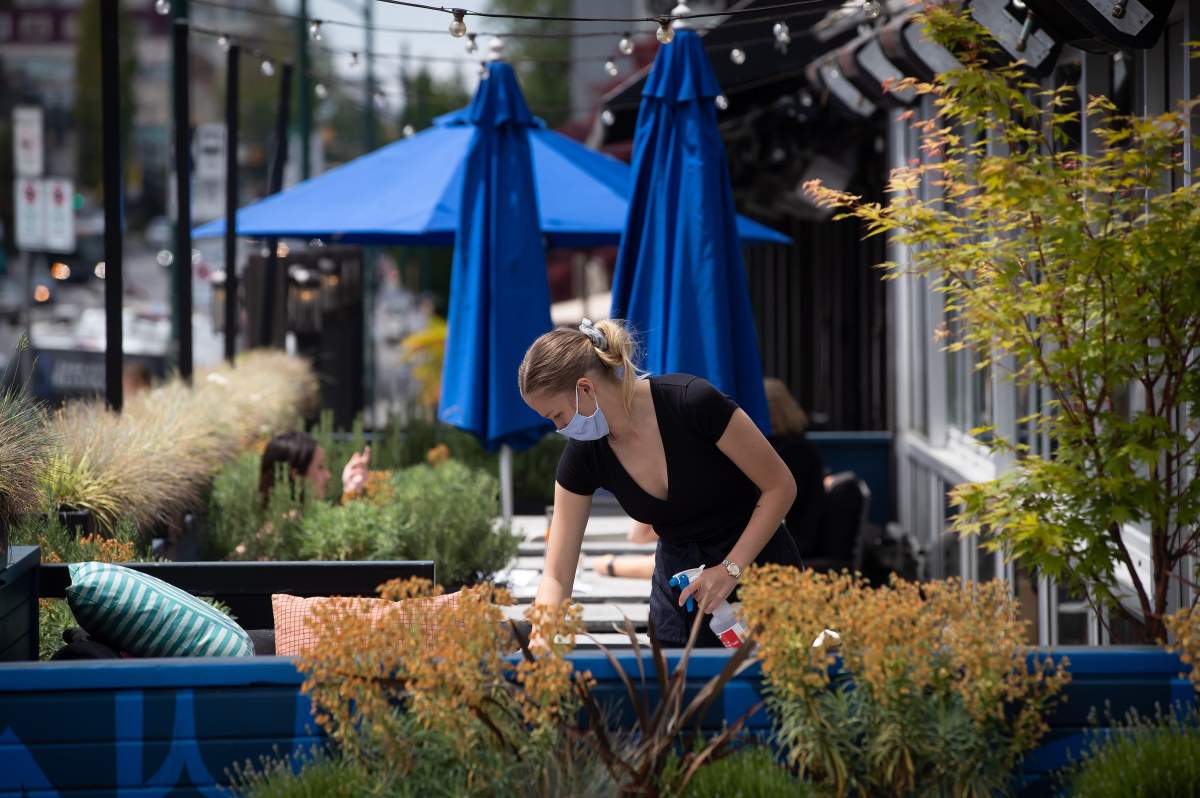 A server wears a face mask while cleaning a table on the patio at an Earls restaurant.