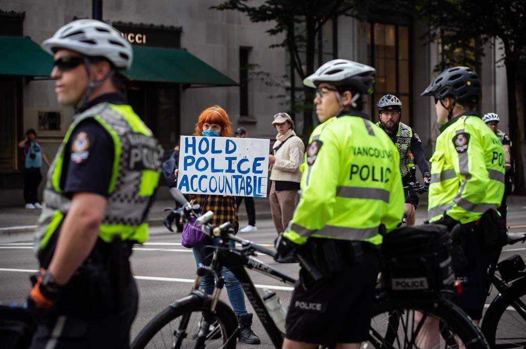 A woman holds a sign reading "Hold Police Accountable" near police officers watching as thousands of people gather for a peaceful demonstration in support of George Floyd and Regis Korchinski-Paquet and protest against racism, injustice and police brutality, in Vancouver, on Sunday, May 31, 2020.