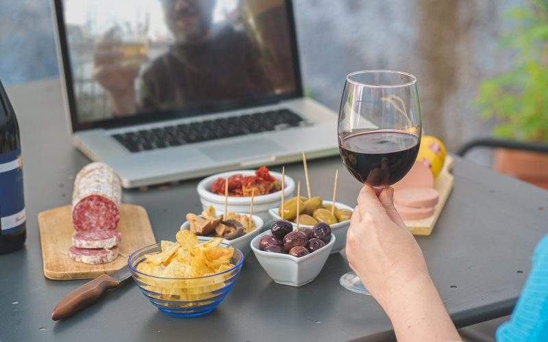 Two people share a drink and some snacks via a virtual meeting. 