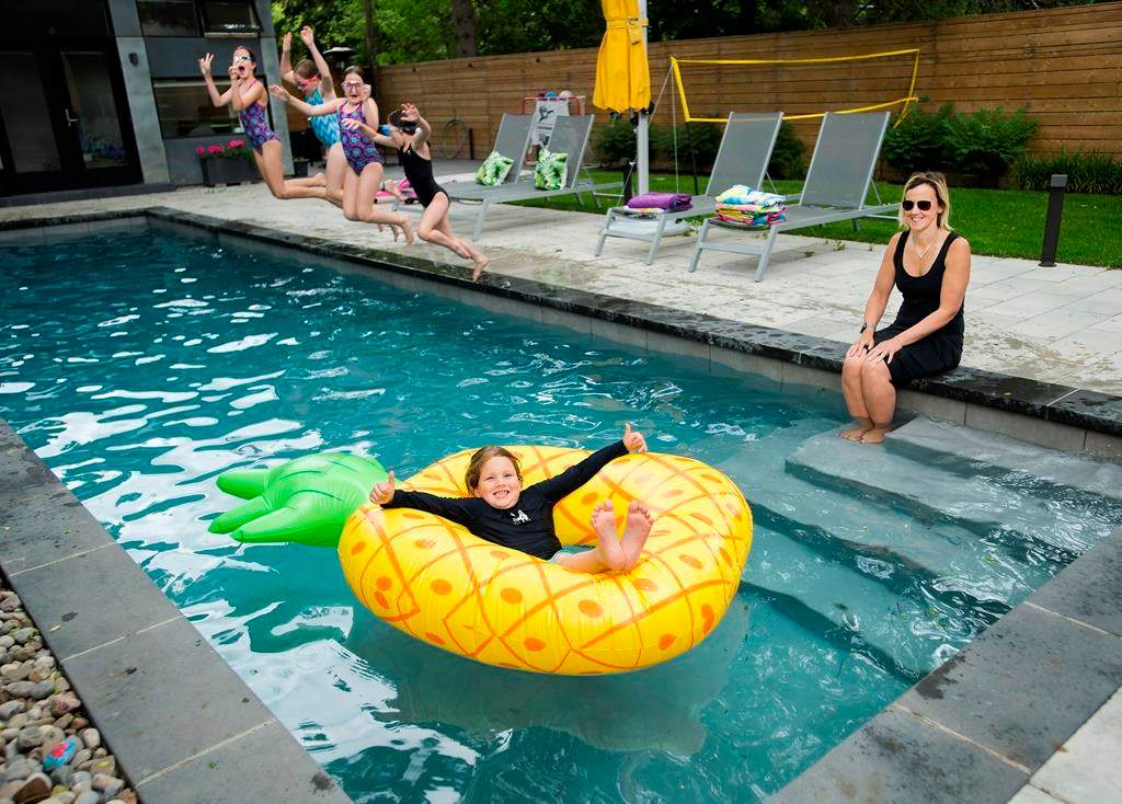 Tory Crowder, right, and her seven-year-old son Stanley, along with his sisters and friends, swim in their swimming pool at their home during the COVID-19 pandemic in Toronto on Wednesday, June 24, 2020. THE CANADIAN PRESS/Nathan Denette.