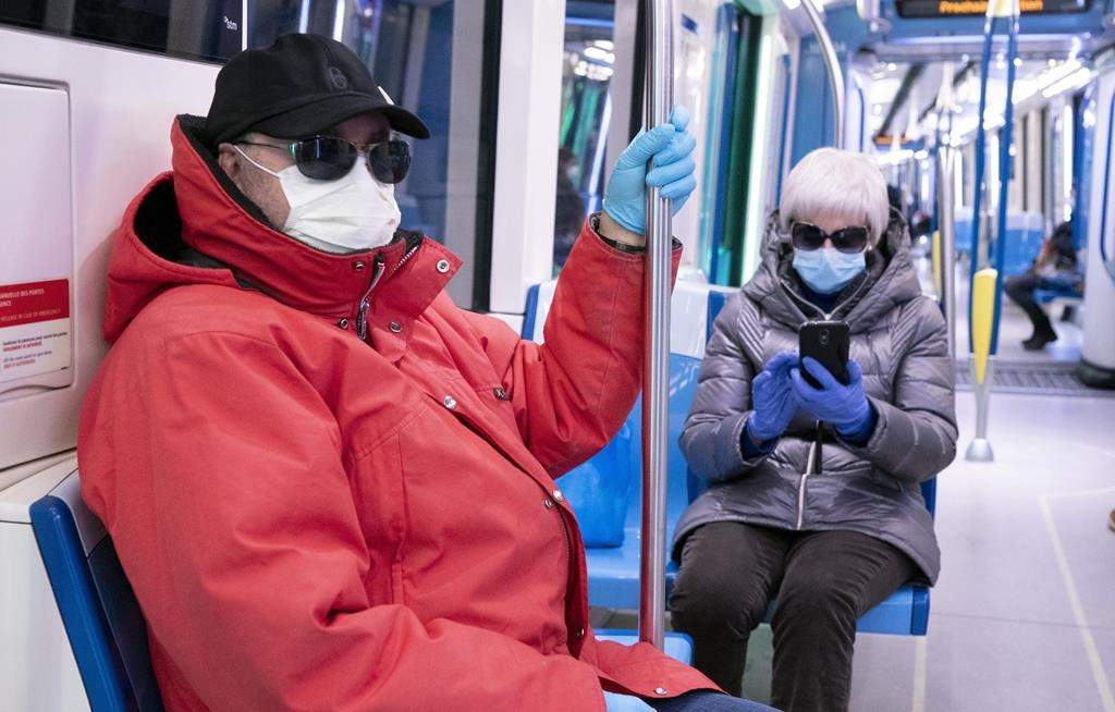 A couple wearing protective masks ride a near-empty subway train in Montreal on Wednesday, April 22, 2020.