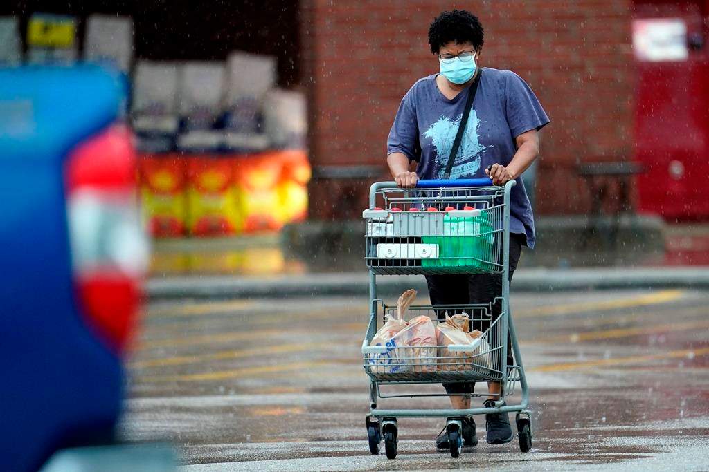 A shopper wears a mask as she pushes her grocery cart in the rain Thursday, June 25, 2020.