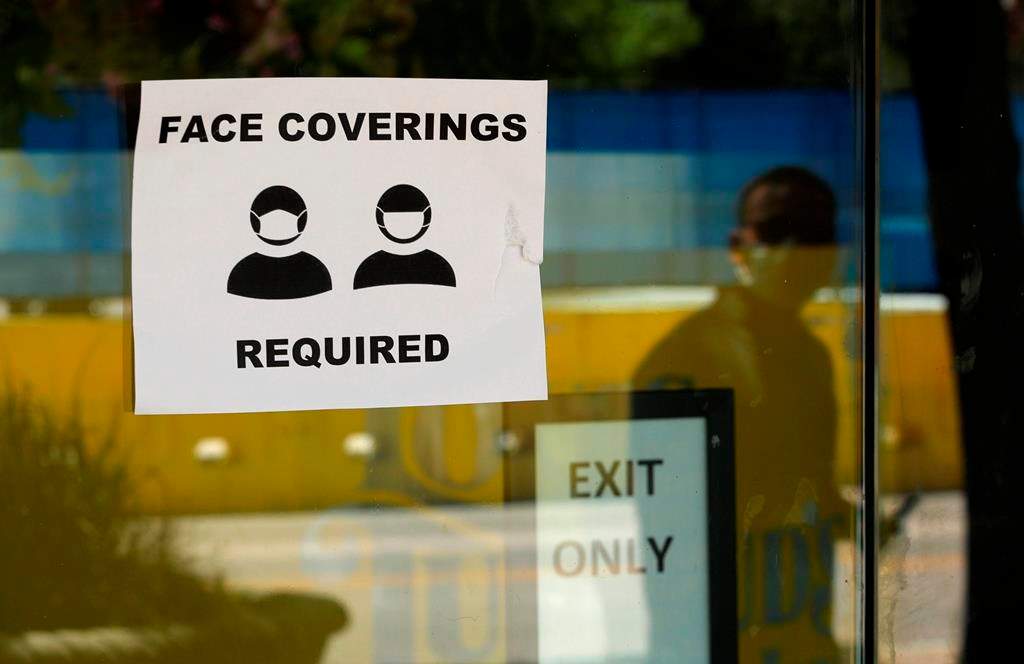 A man wearing mask to protect against the spread of COVID-19 is reflected next to a sign requiring face coverings at a business in San Antonio, Wednesday, June 24, 2020.