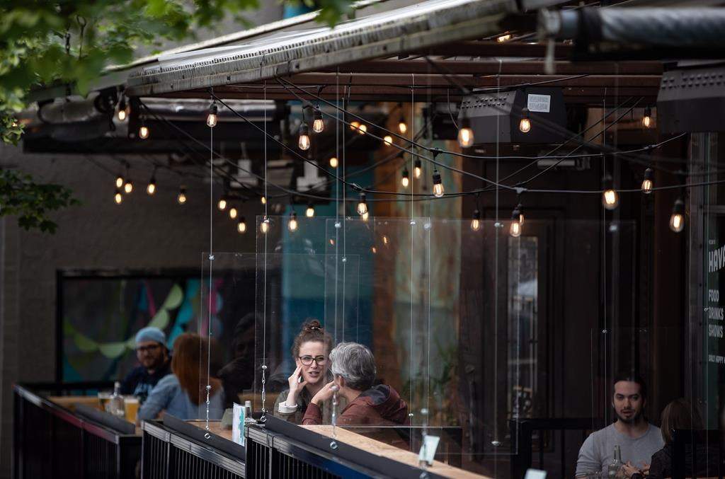 Patrons sit between plexiglass barriers on the patio of a restaurant and bar in Vancouver, on Sunday, May 31, 2020.