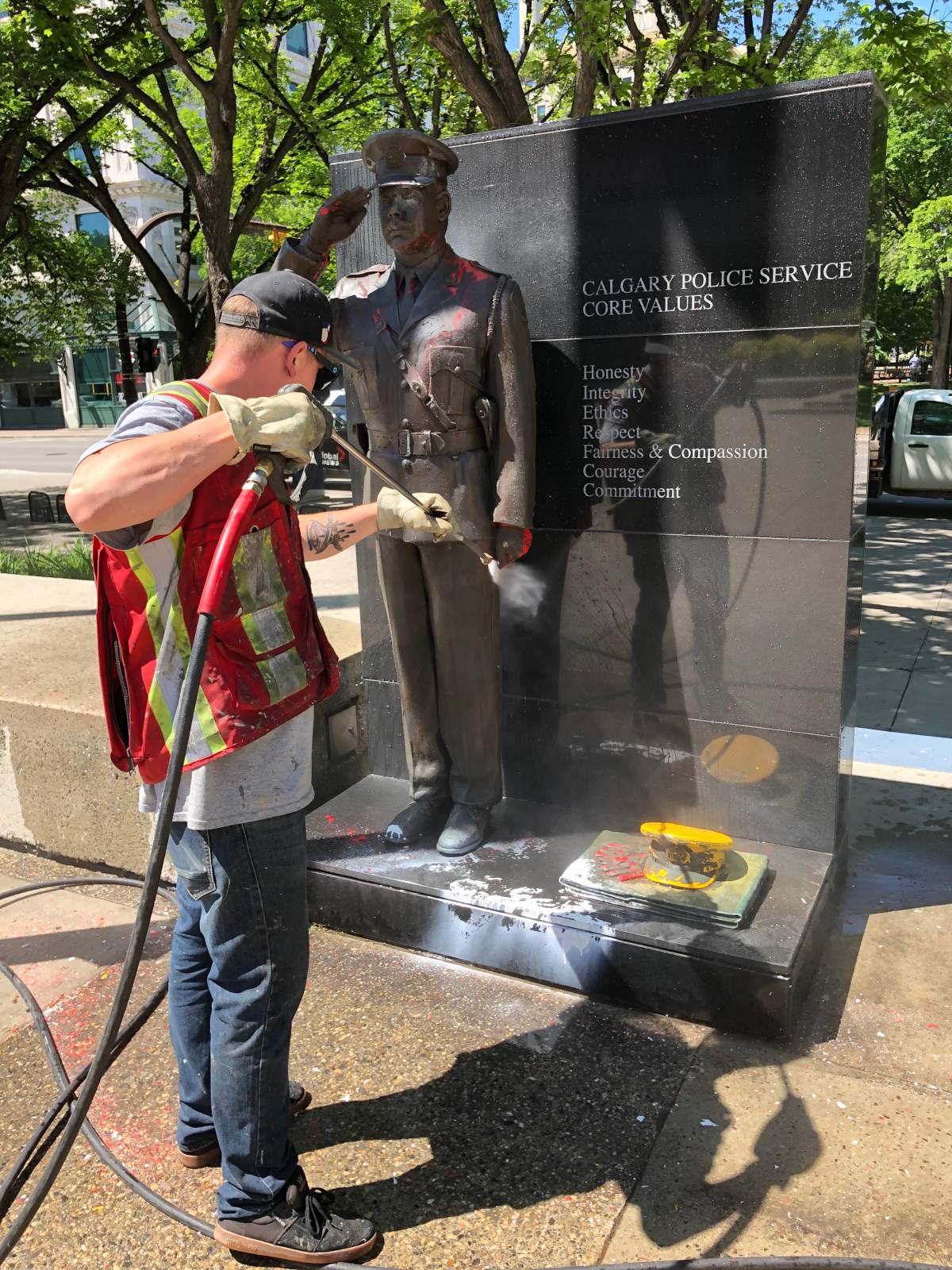 A man is seen pressure washing paint off the statue of a police officer outside Calgary city hall on Friday, July 3.