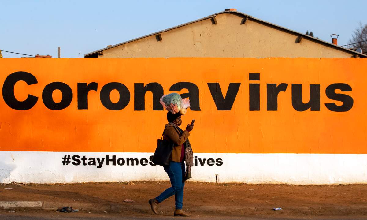 FILE – In this Friday June 19, 2020, a woman wearing a face mask passes a coronavirus billboard carrying a message in a bid to prevent the spread of the virus. (AP Photo/Themba Hadebe/File)