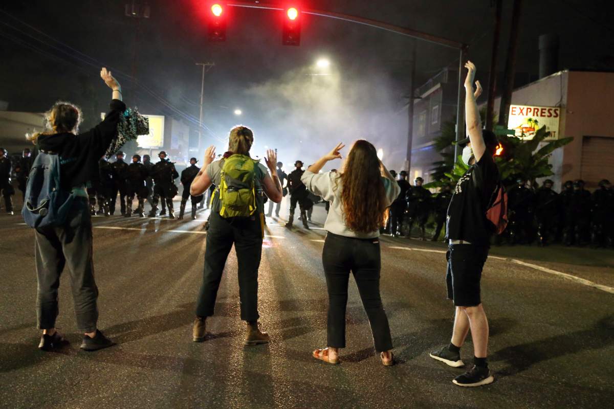 FILE - In this June 30, 2020, file photo, police stand in front of protesters gathered outside Portland Police Union headquarters in Portland, Ore.