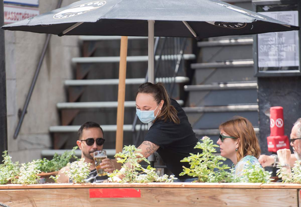 A server wears a face mask as she waits on customers at an outdoor terrace of a taverne in Montreal, Sunday, July 12, 2020.