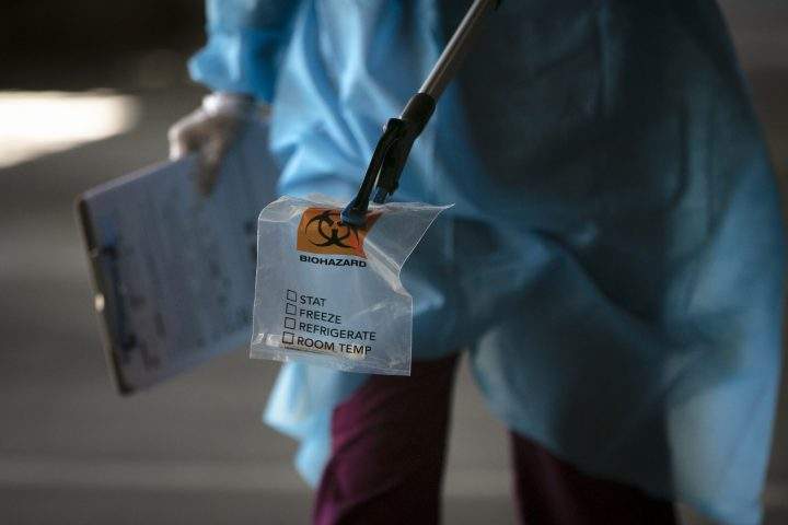 FILE - A physician assistant carries a nasal swab sample using a grabber at a COVID-19 drive-through testing site set up at the Anaheim Convention Center in Anaheim, Calif., Thursday, July 16, 2020.
