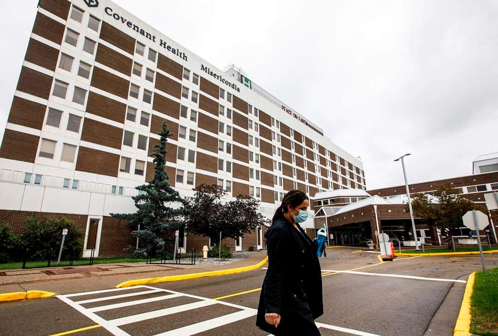 A person wearing a mask walks away from the Misericordia Community Hospital in Edmonton Alta, on Wednesday July 8, 2020. The hospital is no longer admitting patients due to a full outbreak of COVID-19. An outbreak at the Misericordia Community Hospital was first declared by Alberta's chief medical health officer two weeks ago, and restrictions were tightened as case numbers increased. THE CANADIAN PRESS/Jason Franson.
