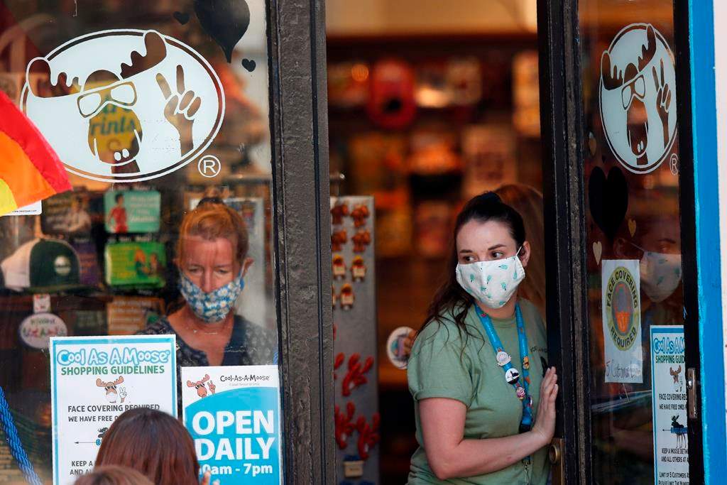 A worker at a gift shop regulated the number of customers allowed in the store due to the coronavirus pandemic, Thursday, July 30, 2020, in Portland, Maine. State officials reported more cases of COVID-19. (AP Photo/Robert F. Bukaty).