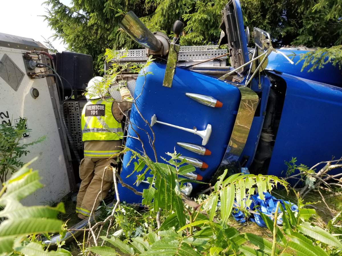 A firefighter is seen attending a flipped over transport truck in the ditch of Hwy 402.