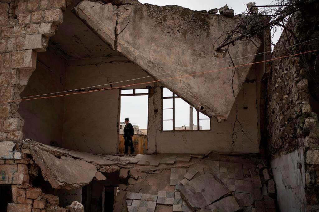 In this Thursday, March 12, 2020 photo, a boy stands inside a house destroyed by an airstrike, in Idlib, Syria.