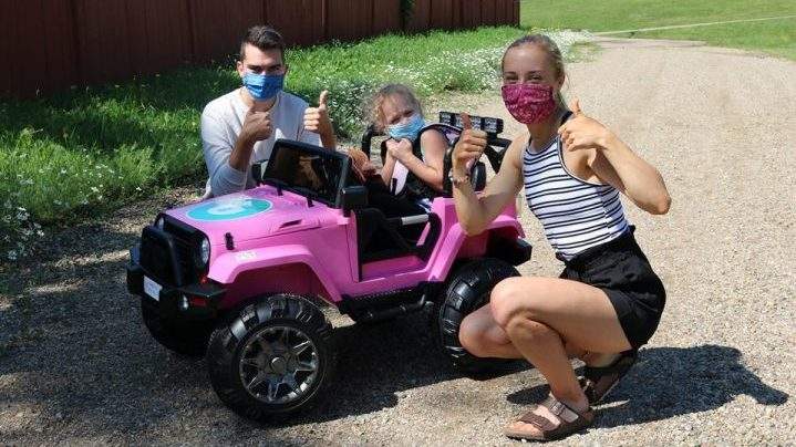 Ryan Sellinger (left) and Robyn Ham (right) of Sask Masks pose with four-year-old Mila Winkler, who they surprised with an adapted toy car on July 24, 2020.
