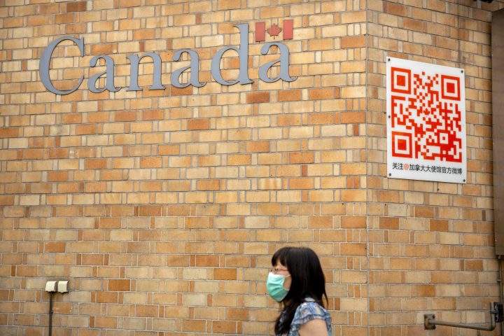 A woman wearing a face mask to help protect against the coronavirus walks past the Canadian Embassy in Beijing, Thursday, Aug. 6, 2020.