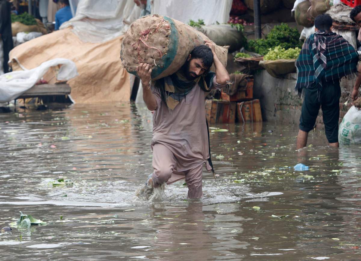 A laborer carries sack of onion while wades through a flooded area after heavy rainfall in Lahore, Pakistan, Thursday, Aug. 20, 2020. Emergency workers say relentless monsoon rains kill some people and injure many in Pakistan’s most populous Punjab province. (AP Photo/K.M. Chaudary)