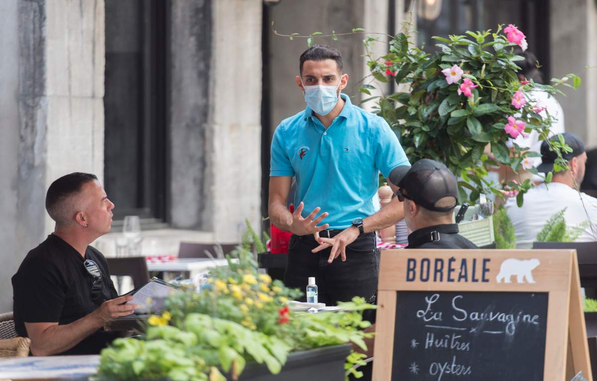 A server wears a face mask as he talks to customers at a restaurant in Montreal, Saturday, Aug. 22, 2020.