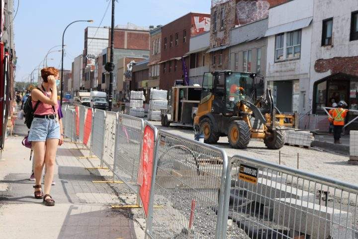 Plaza Saint-Hubert pedestrian glances at construction workers who continue St-Hubert Street’s roadwork on Tuesday, Aug. 11, 2020.