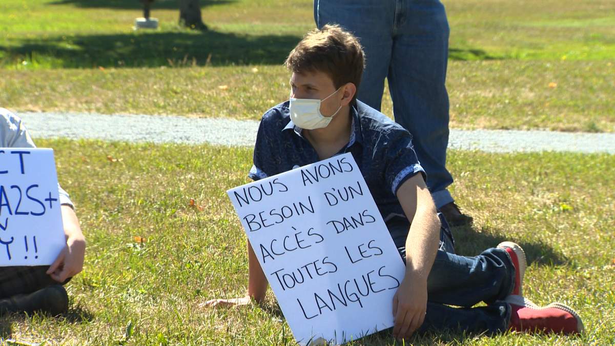 “We need access in all languages,” reads one sign at the rally.