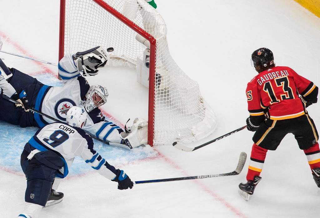 Winnipeg Jets goalie Connor Hellebuyck (37) is scored on by the Calgary Flames' Johnny Gaudreau (13) as the Jets' Andrew Copp defends during second-period NHL qualifying round game action in Edmonton, on Saturday, Aug. 1, 2020.