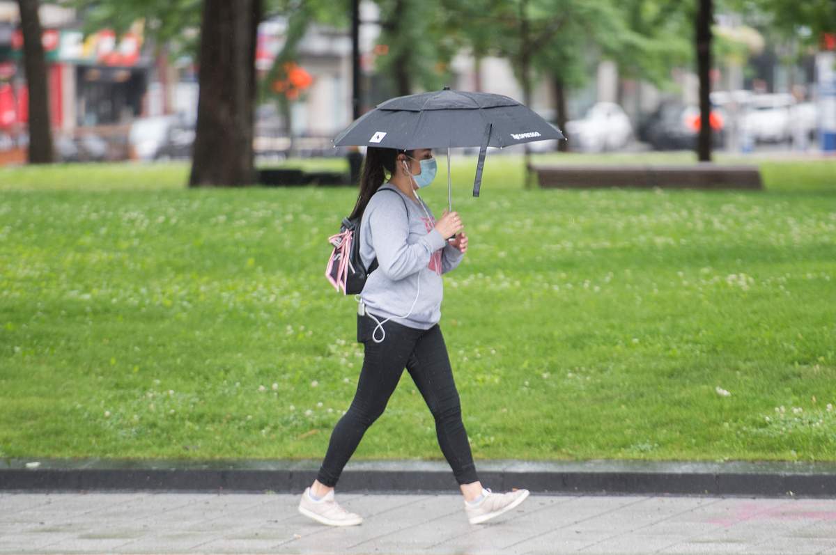 A woman wears a face as she walks along a street in the rain in Montreal, Saturday, July 11, 2020, as the COVID-19 pandemic continues in Canada and around the world. 