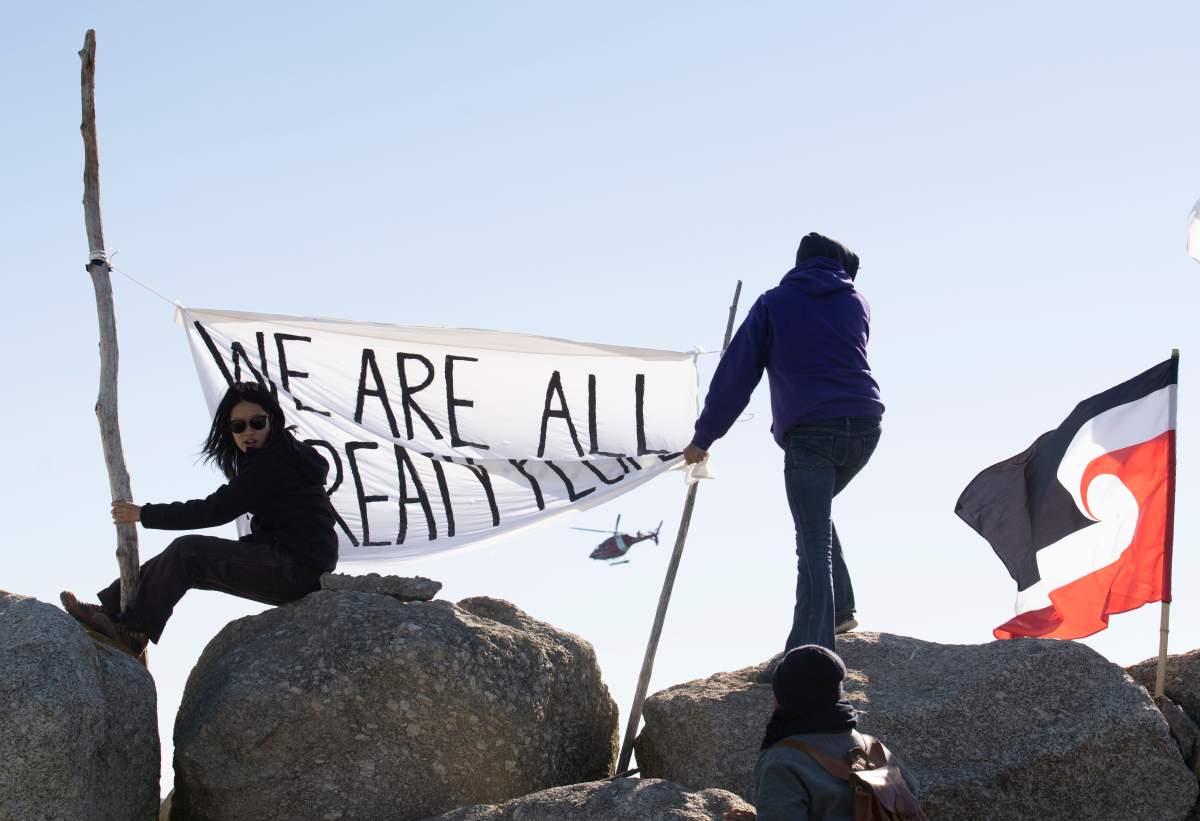 Sipekne’katik First Nation community members wave a flag that reads ‘We are all treaty people’, while a coast guard helicopter hovers in the background in Saulnierville, N.S. on Sunday, September 20, 2020.