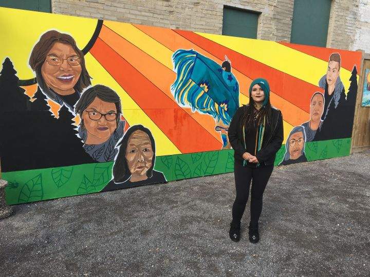 Tristen Jenni Sanderson stands in front of the large mural she created at the Boyle Street Community Services centre in downtown Edmonton.