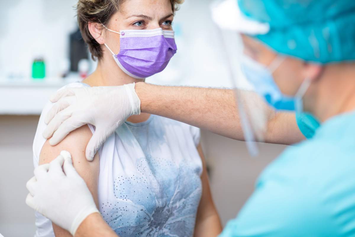 Female patient with protective face mask waiting for vaccination, doctor in surgical gloves disinfecting her arm.