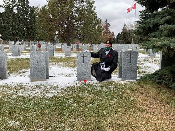 Brian Phelan sits next to his father’s gravestone holding the Canadian Efficiency Medal.