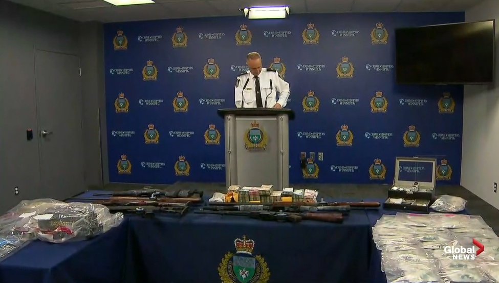 Insp. Max Waddell stands behind some of the weapons and drugs found in two raids in June.