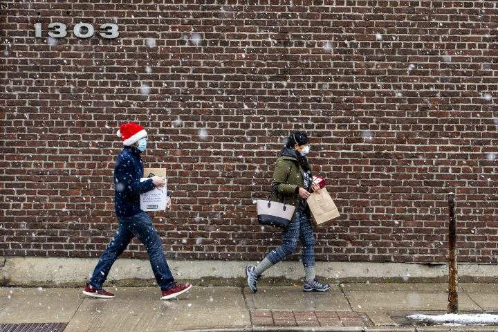 People walk along Queen Street West as snow falls in Toronto on Sunday, Nov. 22, 2020. 