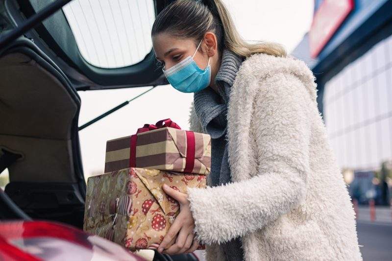 Teenage girl packing Christmas gifts in a car after shopping. She wears a protective mask to protect from corona virus COVID-19.