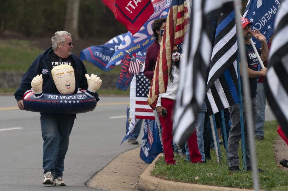 A person in an inflatable toy supporting United States President Donald Trump joins protesters demonstrate as Trump golfs at Trump National Golf Club. 