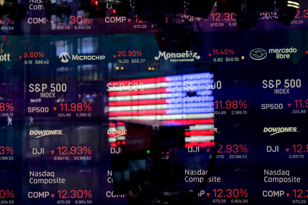 A United States flag is reflected in the window of the Nasdaq studio, which displays indices and stocks down, in Times Square, New York, Monday, March 16, 2020. 