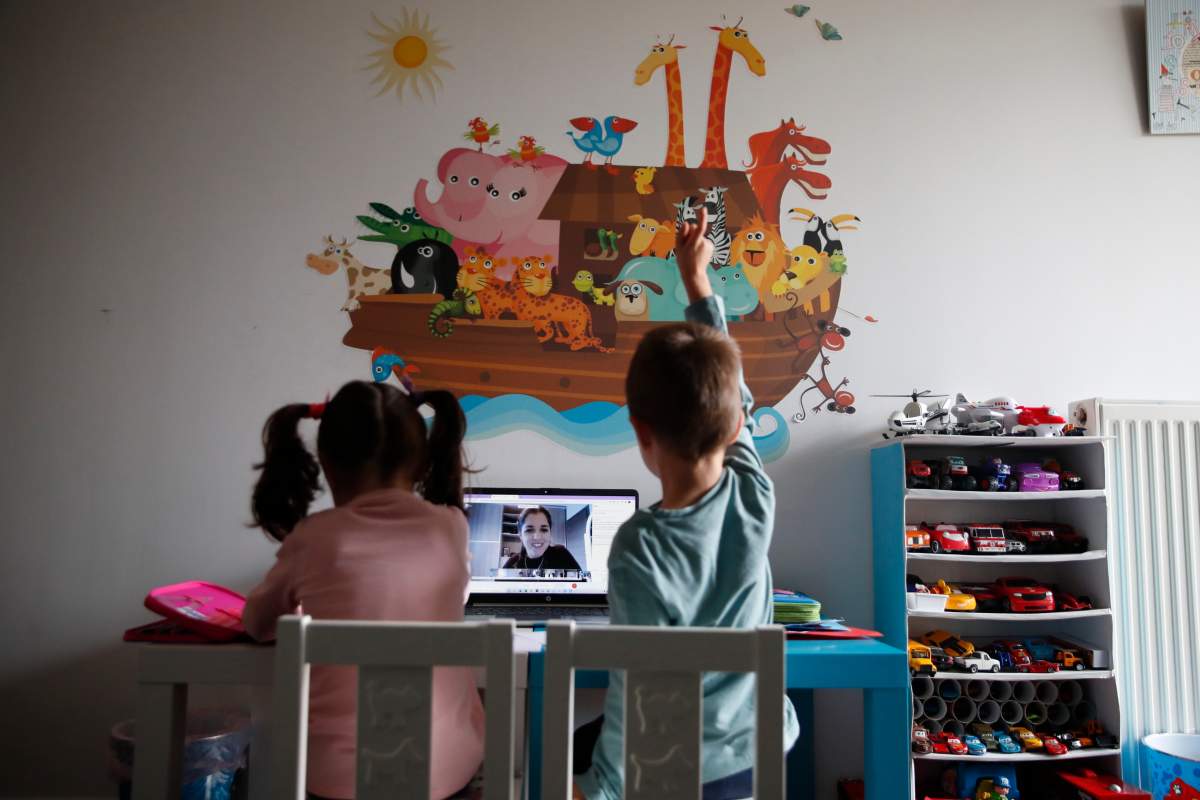 A kindergarten teacher reads a fairy story as Panos raising his hand with his twin sister Marina watch the online lesson in Athens, Greece. Thursday, Nov. 19, 2020. (AP Photo/Thanassis Stavrakis).