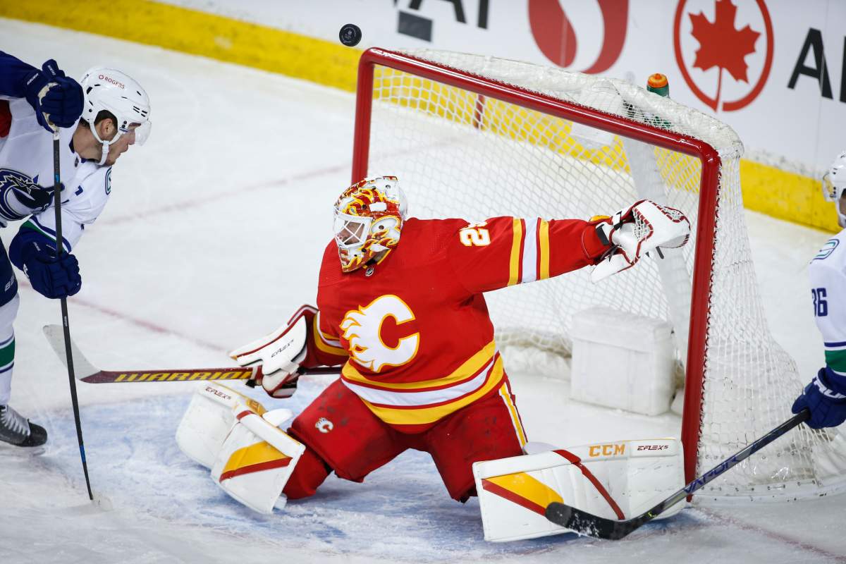 Vancouver Canucks' Bo Horvat, left, looks on as the puck passes over Calgary Flames goalie Jacob Markstrom during first period NHL hockey action in Calgary, Saturday, Jan. 16, 2021.