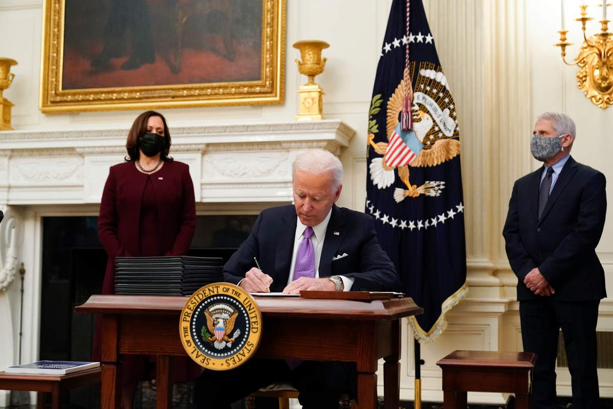 President Joe Biden signs executive orders after speaking about the coronavirus, accompanied by Vice President Kamala Harris, left, and Dr. Anthony Fauci, director of the National Institute of Allergy and Infectious Diseases, right, in the State Dinning Room of the White House, Thursday, Jan. 21, 2021, in Washington.