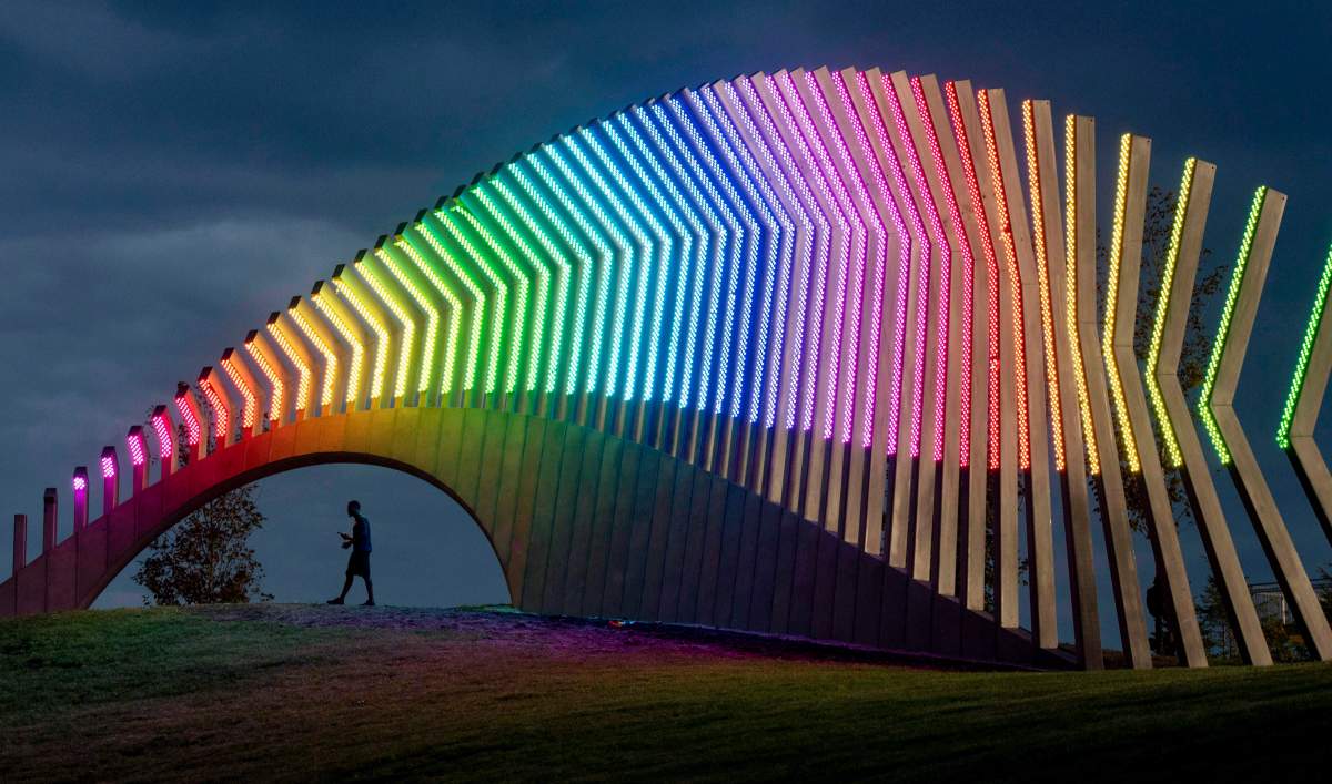 A man walks under Moving Surfaces, a giant steel and light sculpture at Ottawa's Lansdowne Park, as it is lit up in the colours of the rainbow, during Pride Week on Saturday, Aug. 25, 2018.