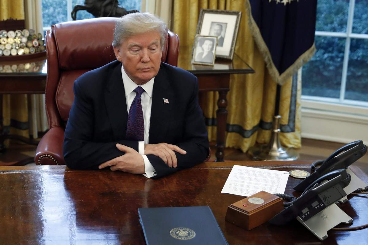 U.S. President Donald Trump eyes his Diet Coke button at the Resolute Desk in the Oval Office of the White House in Washington, Tuesday, Jan. 23, 2018.